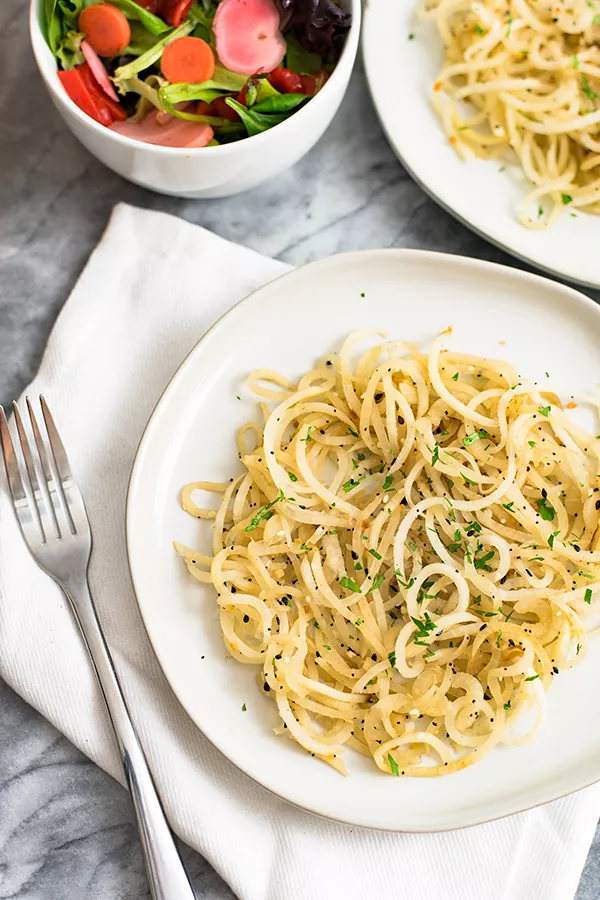 white bowl with low carb pasta made of daikon radish with parsley on top with a fork on a white napkin