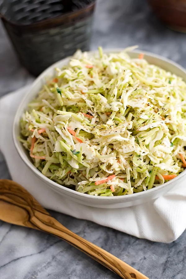 Large white bowl filled with paleo coleslaw over a white napkin and a wooden spoon.