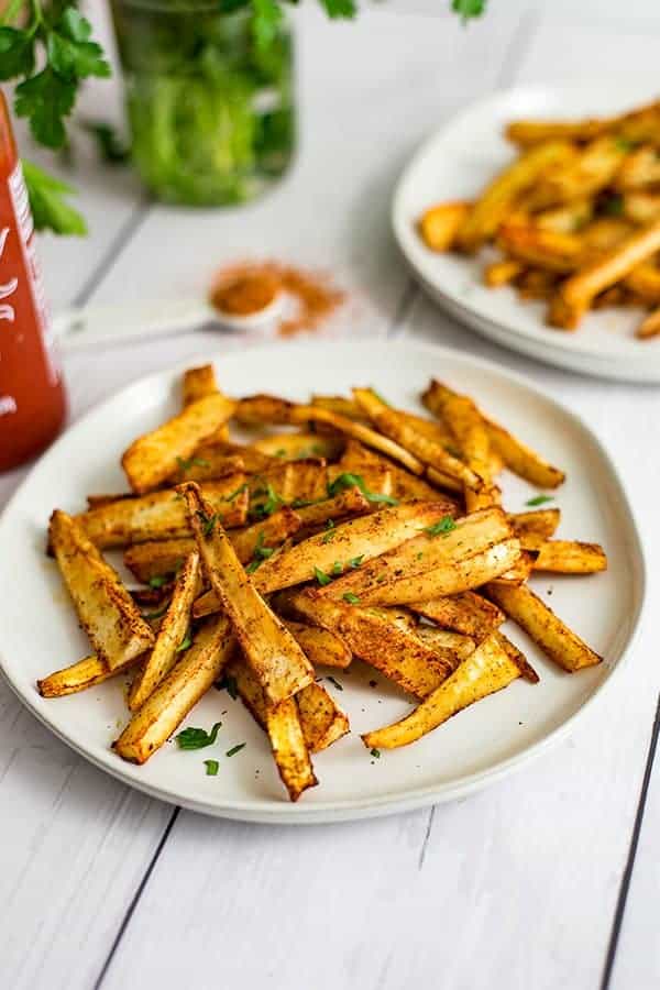 Cajun parsnip fries on a white plate with cajun seasoning in a measuring spoon 