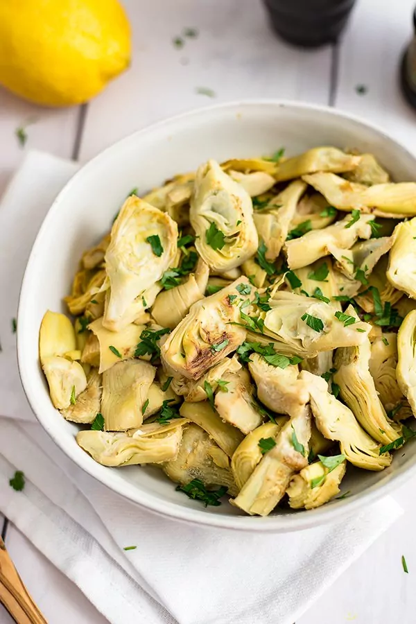 Large bowl filled with lemon artichokes with lemon in the background