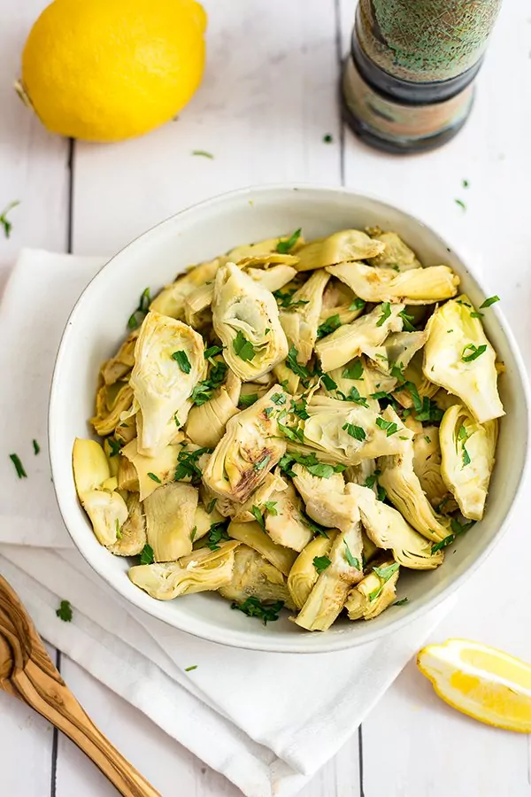 Bowl filled with lemon artichoke and chopped parsley over a white napkin