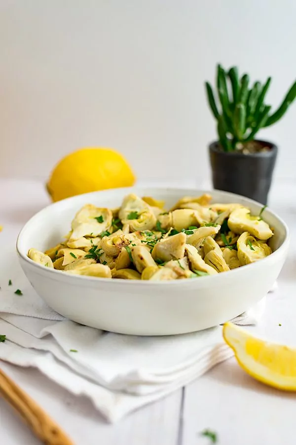 White bowl filled with lemon artichoke recipe. succulent plant in background