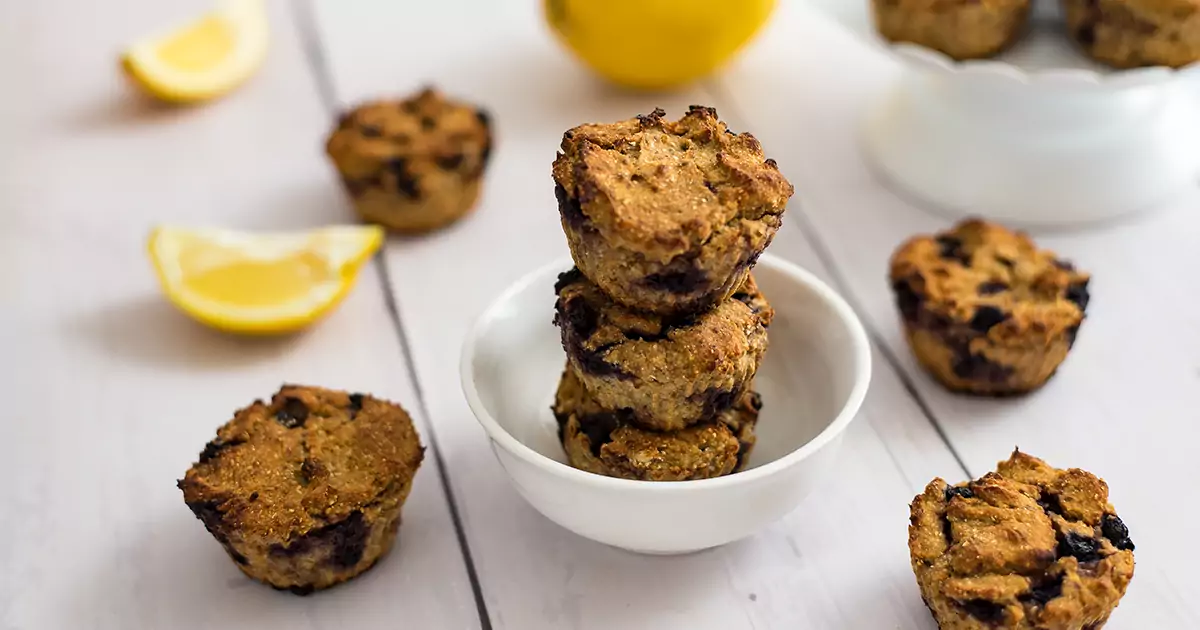 Three lemon blueberry muffins stacked on top of each other in a white bowl.