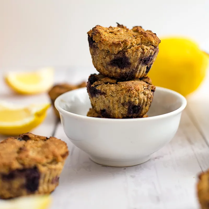 Two lemon blueberry muffins in a white bowl with a lemon in the background