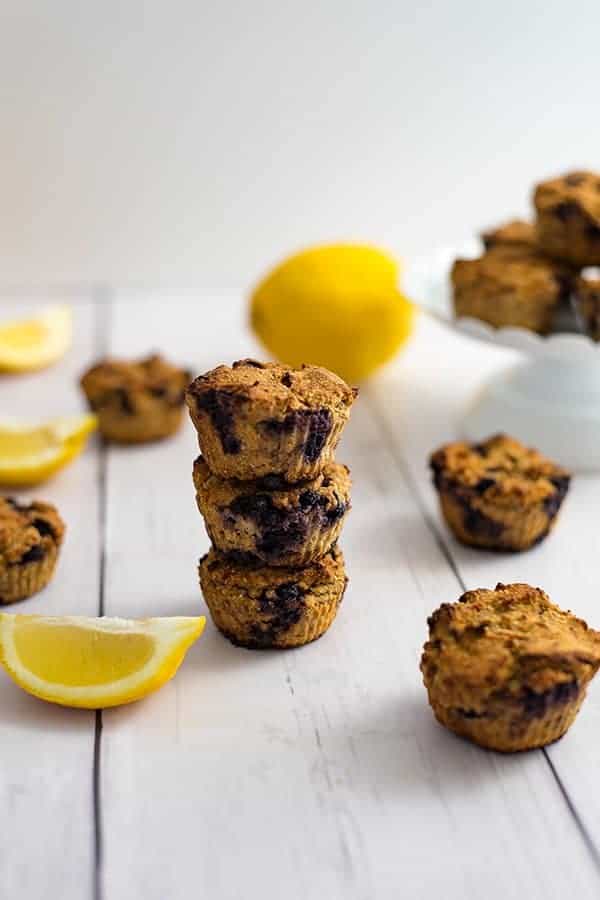Three lemon blueberry muffins stacked on top of eachother with lemon blueberry muffins and lemons in the background
