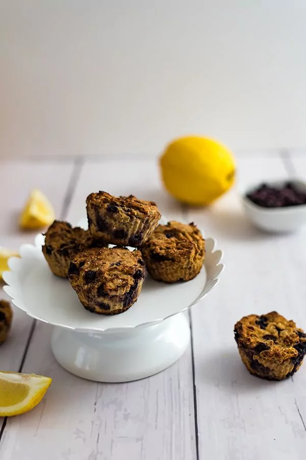 Lemon Blueberry muffins on a white cake platter with a lemon in the background