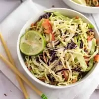 White bowl of spicy creamy asian slaw with a lime in the bowl, with chop sticks on the left side