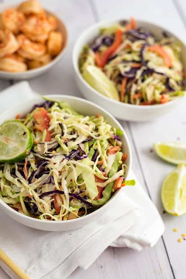 Two white bowls filled with spicy creamy asian slaw with a bowl of shrimp in the background 