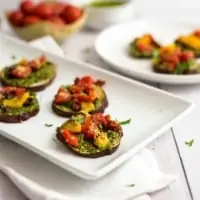 Sweet potato pizza bites on a white plate with a bowl of tomatoes in the background.