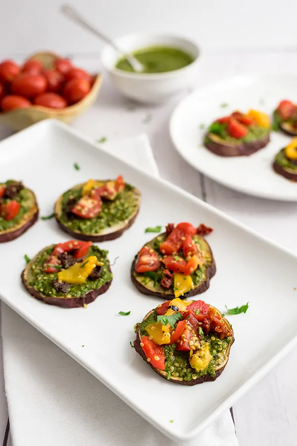 Sweet potato pizza bites on a white rectangular plate with tomatoes and pesto in the background.
