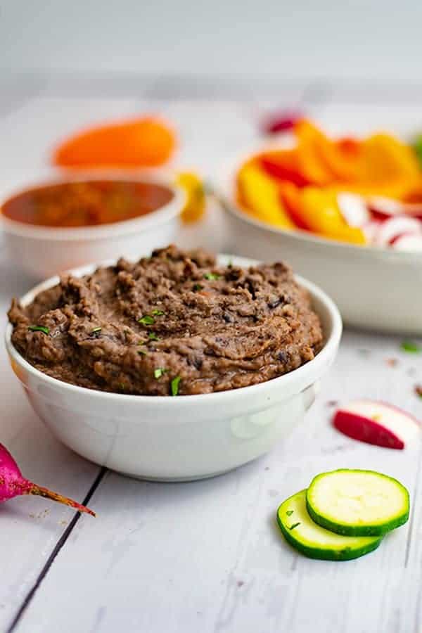 White bowl full of 3 ingredient black bean dip recipe with sliced veggies in the background