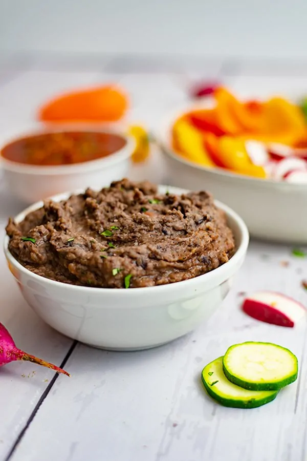 White bowl full of 3 ingredient black bean dip recipe with sliced veggies in the background