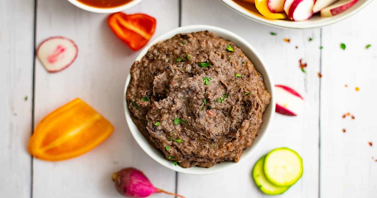 Overhead shot of 3 ingredient black bean dip recipe with radishes, peppers and zucchini slices around the bowl