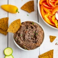 Overhead shot of a bowl of the 3 ingredient black bean dip recipe with a chip in the dip and chips around the bowl.