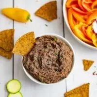 Overhead shot of a bowl of the 3 ingredient black bean dip recipe with a chip in the dip and chips around the bowl.