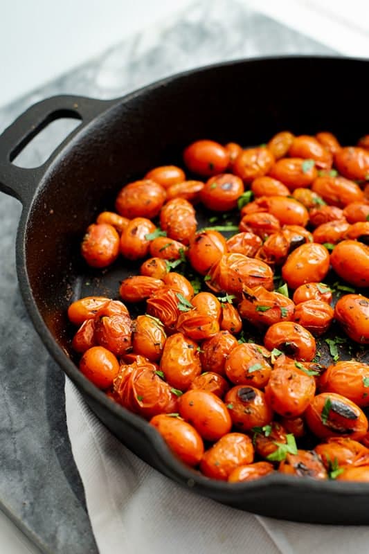 Cast iron skillet with blistered tomatoes over a white napkin