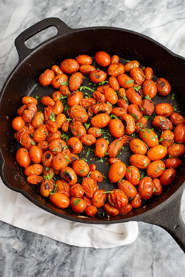 Overhead shot of a cast iron skillet filled with blistered tomatoes