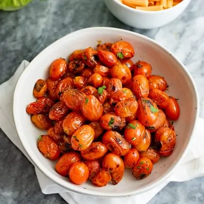 Overhead shot of a large white bowl of blistered tomatoes topped with parsley