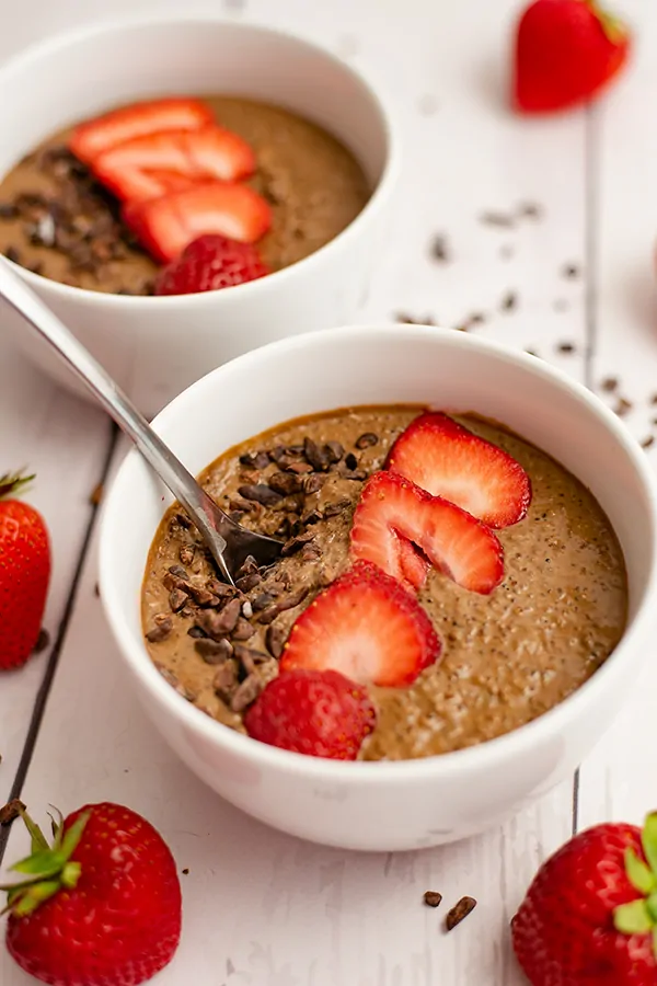 Breakfast quinoa bowl recipe topped with cacao nibs and strawberries, with a spoon in the bowl. 