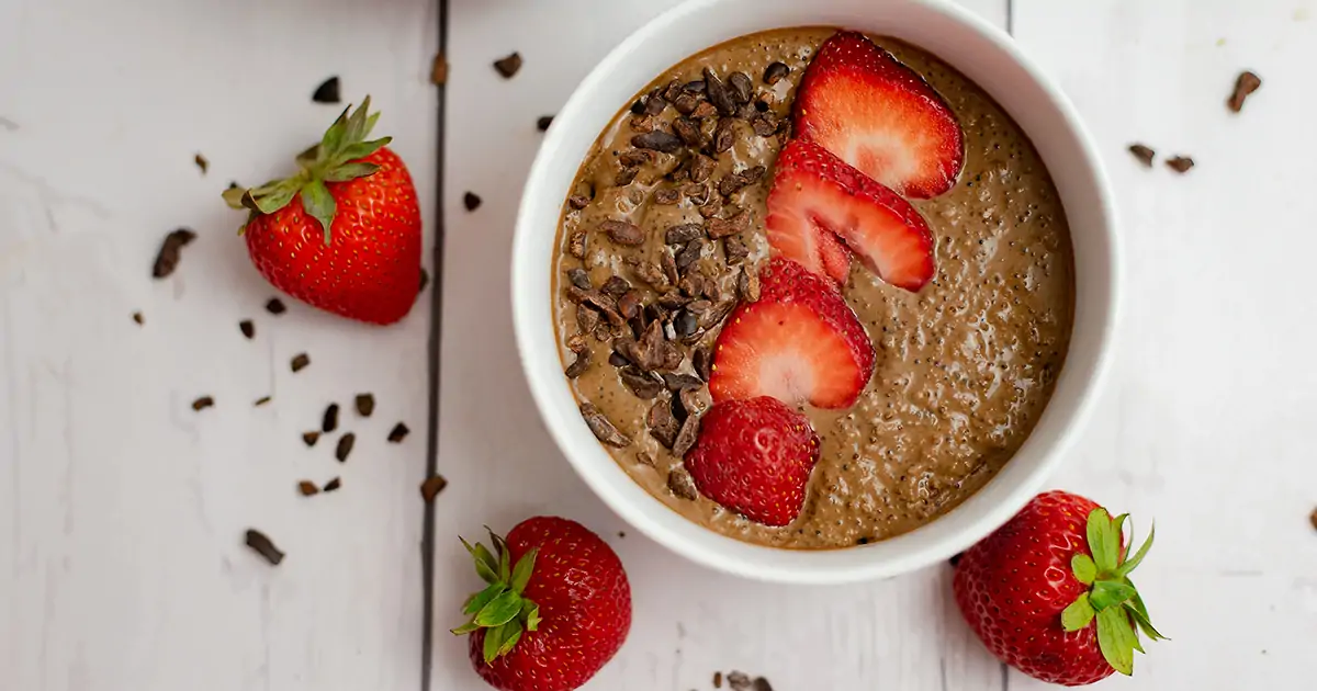 Breakfast quinoa bowl recipe in a white bowl surrounded by strawberries and cacao nibs.