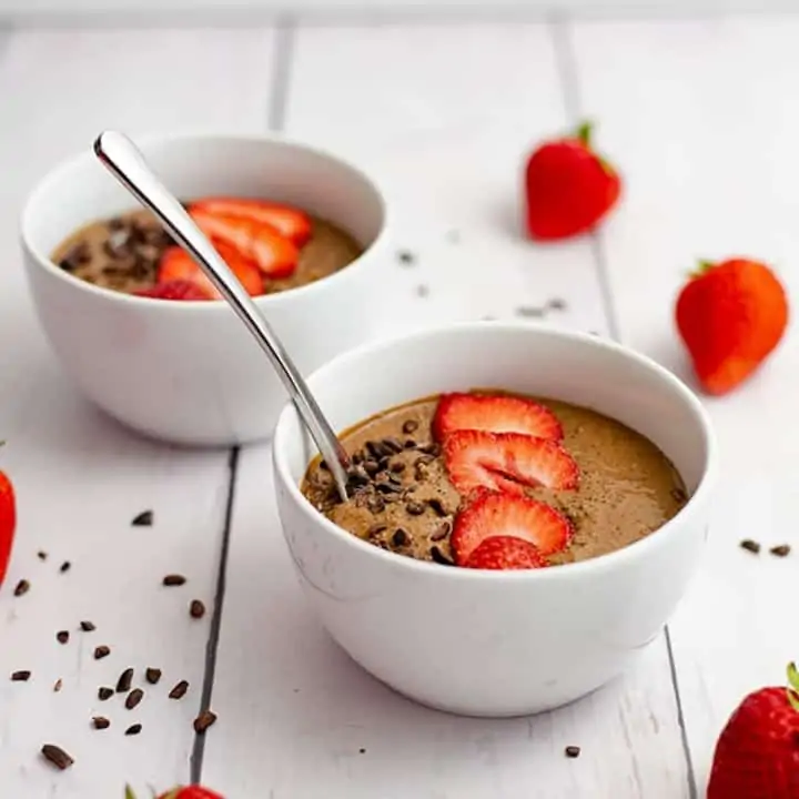 Two white bowls filled with the breakfast quinoa bowl recipe. Topped with strawberries and cacao nibs.