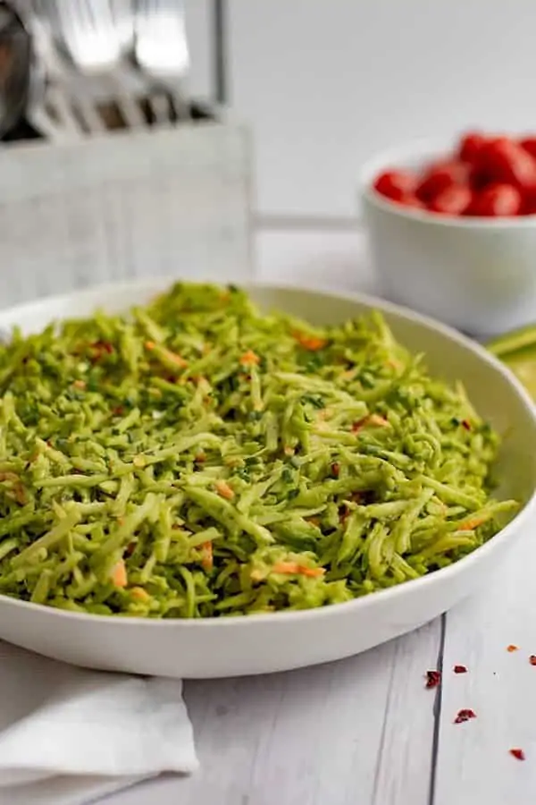 This large bowl of broccoli slaw salad with avocado ranch dressing in a white bowl with a bowl of tomatoes in the background