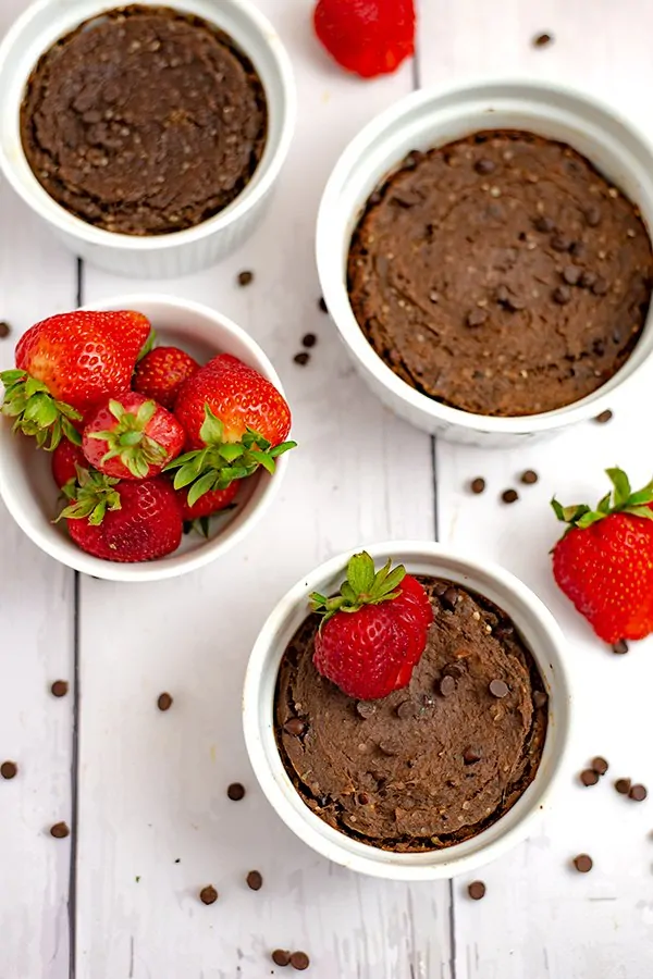 overhead shot of two single serve brownies in white ramekins with a bowl of strawberries on the side