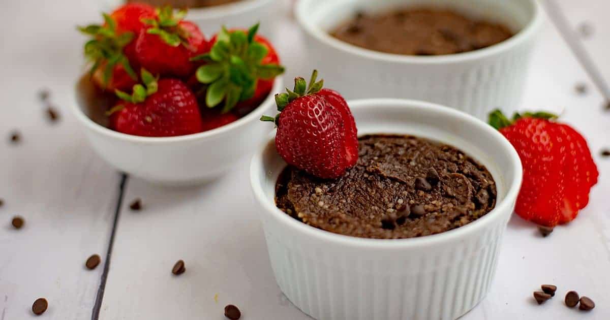 Two single serve brownies in white ramekins surrounded by strawberries