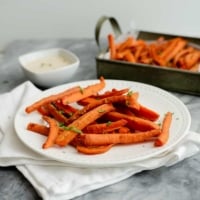 spicy curry oven baked carrot fries on a white plate and a white napkin with a small ramekin of lime cilantro tahini sauce in the background