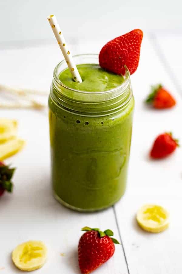 A large mason jar full of the strawberry banana green smoothie with a straw in the drink and a strawberry on the rim.