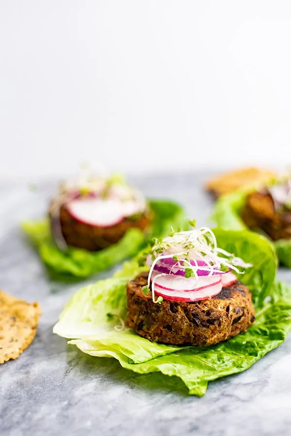 Vegan Black bean burger recipe over lettuce leaves topped with sliced radish, red onion and sprouts.