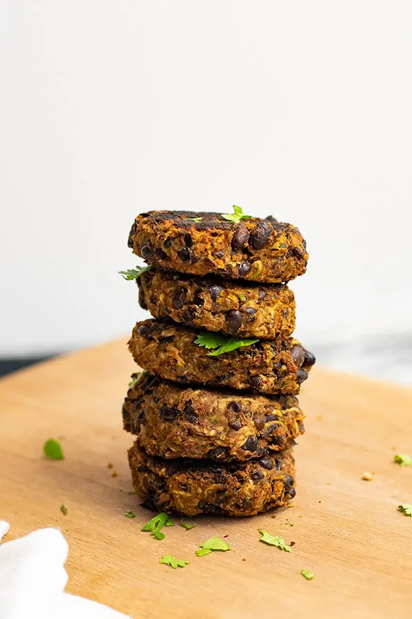 5 Ingredient black bean burger recipe stacked 5 high on a wooden cutting board. 