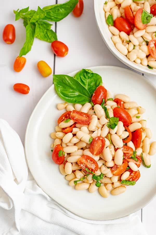 Small plate of vegan cannellini bean salad with a large bowl of the salad in the background.