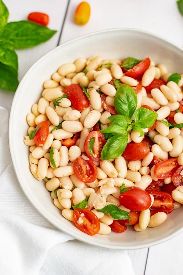Overhead shot of the large white bowl filled with vegan cannellini bean salad topped with fresh basil.