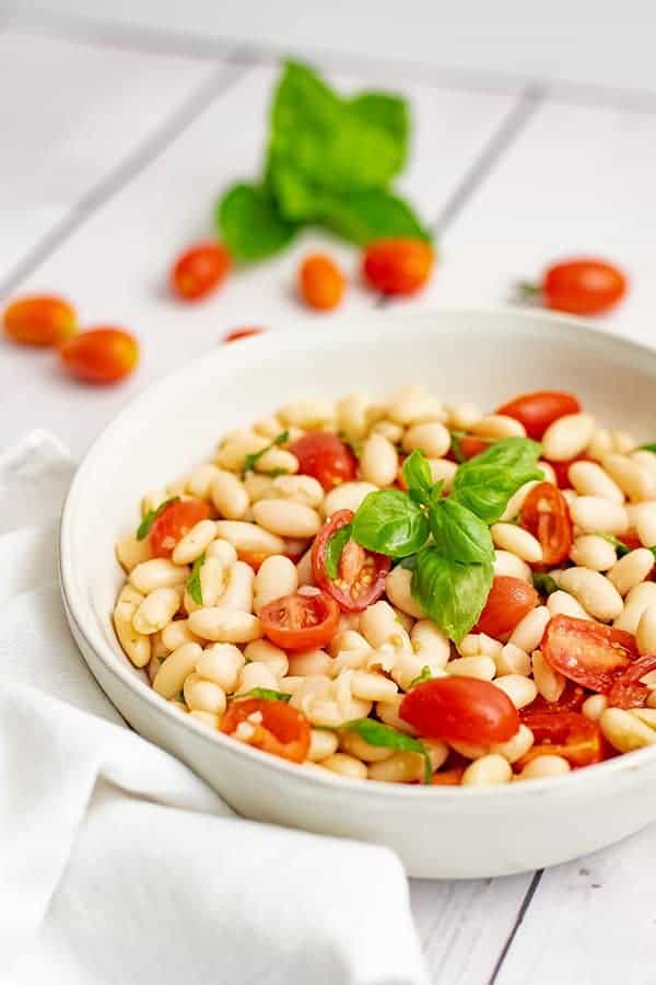 Large bowl filled with vegan cannellini bean salad with a white napkin on the side. 
