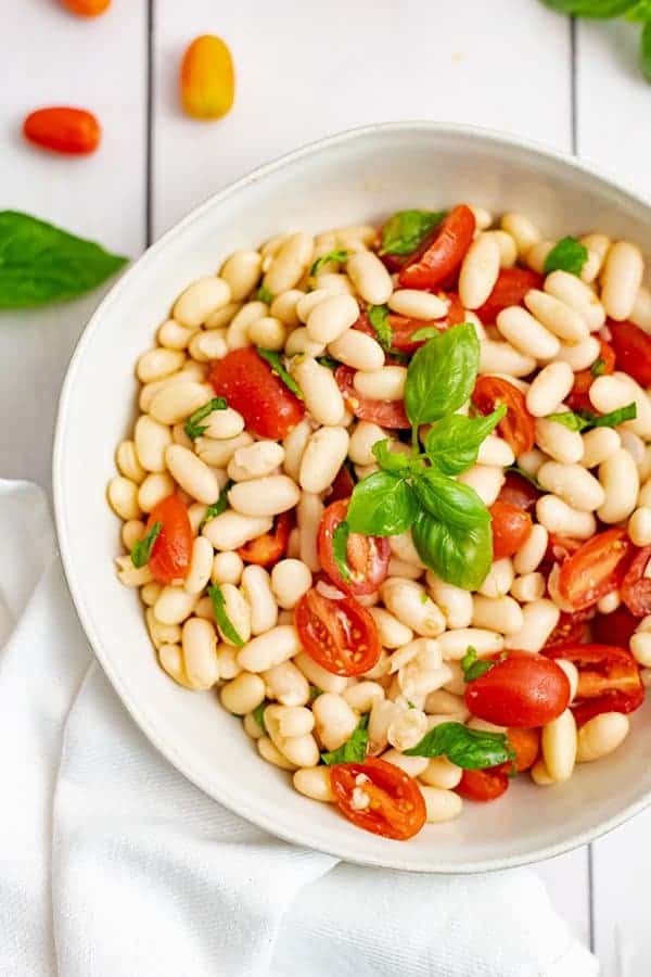 Vegan cannellini bean salad with fresh basil leaves on top in a white bowl. 