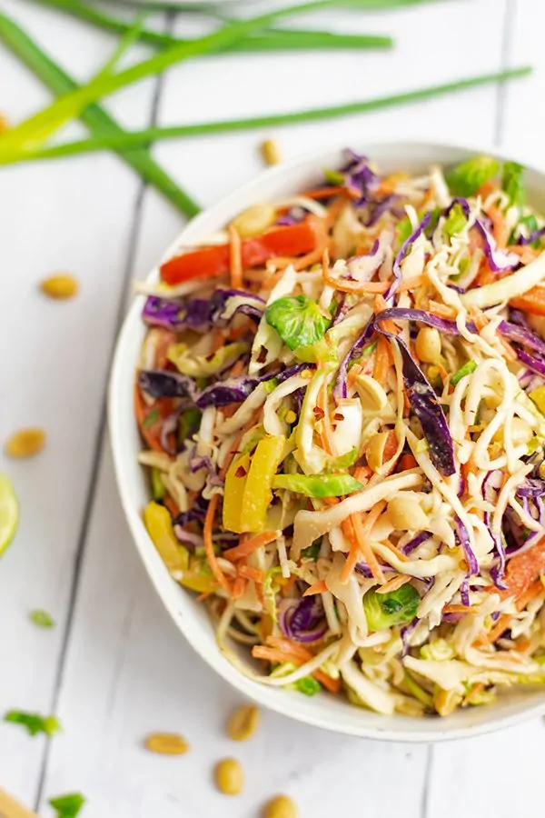 Large white bowl of Asian slaw salad with peanut dressing, green onions in background. 