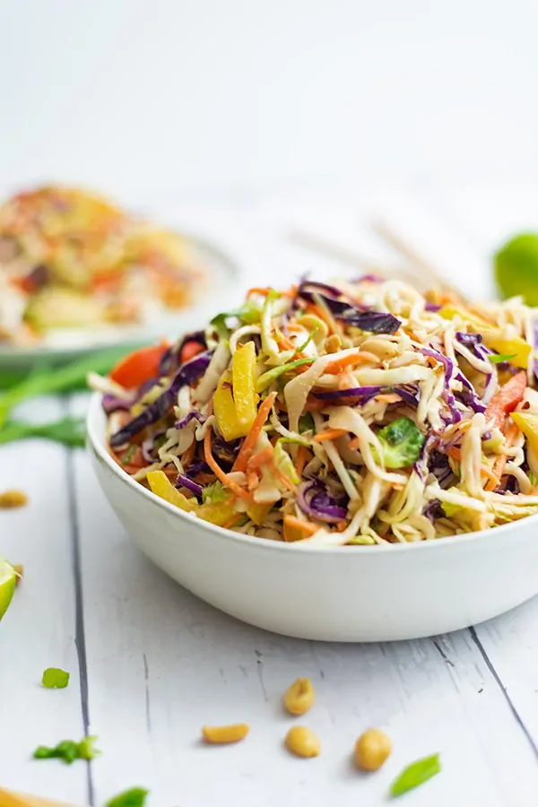 White bowl filled with Asian Cabbage Slaw with a second plate of Asian Cabbage slaw in the background, blurred. 