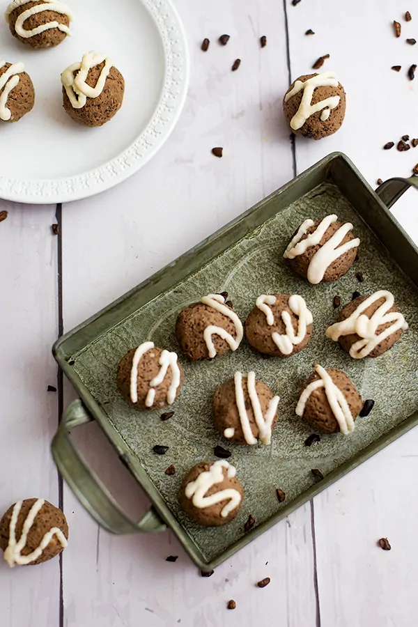 Mocha quinoa energy bites with coconut frosting over a green tray and a small white plate with additional energy bites in the background