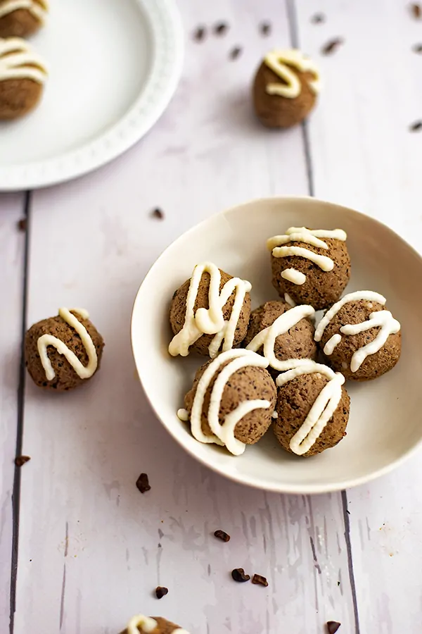 Small white bowl full of mocha quinoa energy bites surrounded by cacao nibs