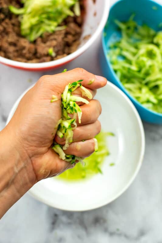 Zucchini shreds being squeezed out by hand.