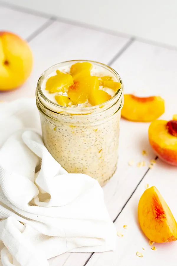 Small mason jar filled with peach overnight oats with yogurt with sliced peaches on top with sliced peaches surrounding the jar