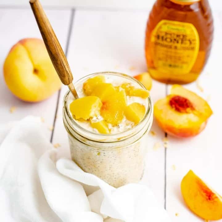 Small mason jar filled with peach overnight oats with yogurt with sliced peaches on top and a brown handled spoon in the top.