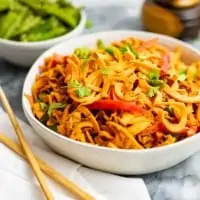 spicy peanut spiralized sweet potatoes in a large white bowl with chopsticks to the left side and green snap peas in the background
