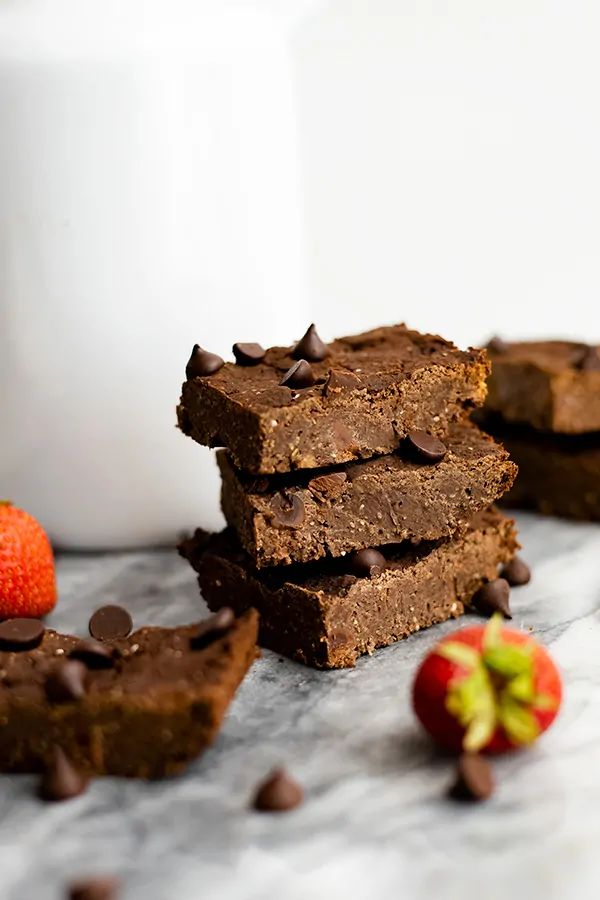 Three vegan black bean brownies with a strawberries and single brownies around them on a marble slab. 