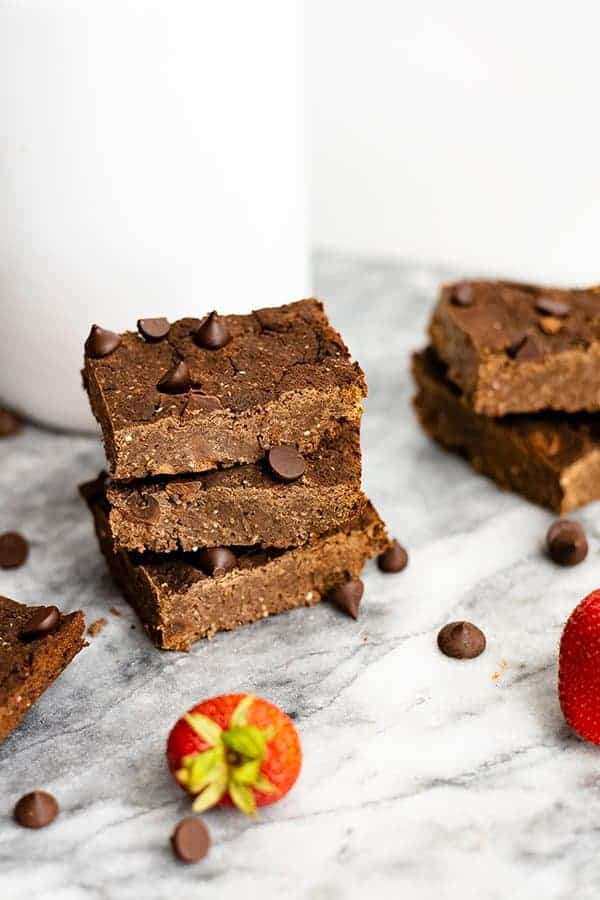 Three vegan black bean brownies stacked on top of each other with a strawberry and chocolate chips in the forefront. 
