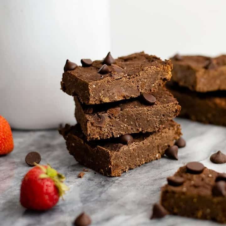 Close up shot of Three vegan black bean brownies with a strawberries and single brownies around them on a marble slab.