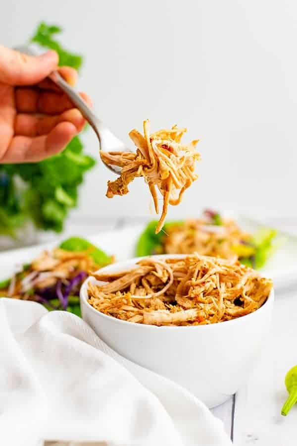 Whole30 slow cooker cajun chicken recipe shredded in a large white bowl with a fork filled with shredded jerk chicken above the bowl. 