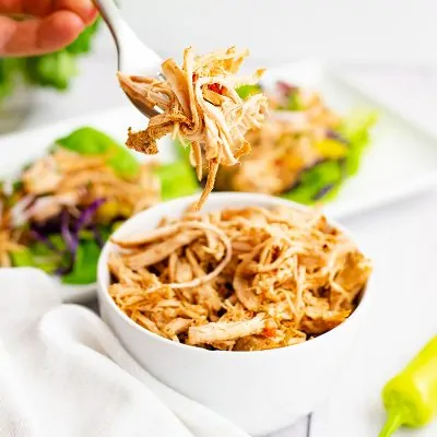 Whole30 slow cooker cajun chicken recipe shredded in a large white bowl with a fork filled with shredded jerk chicken above the bowl.