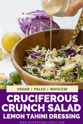 Wooden bowl filled with cruciferous crunch salad with jar of lemon tahini dressing being poured onto it